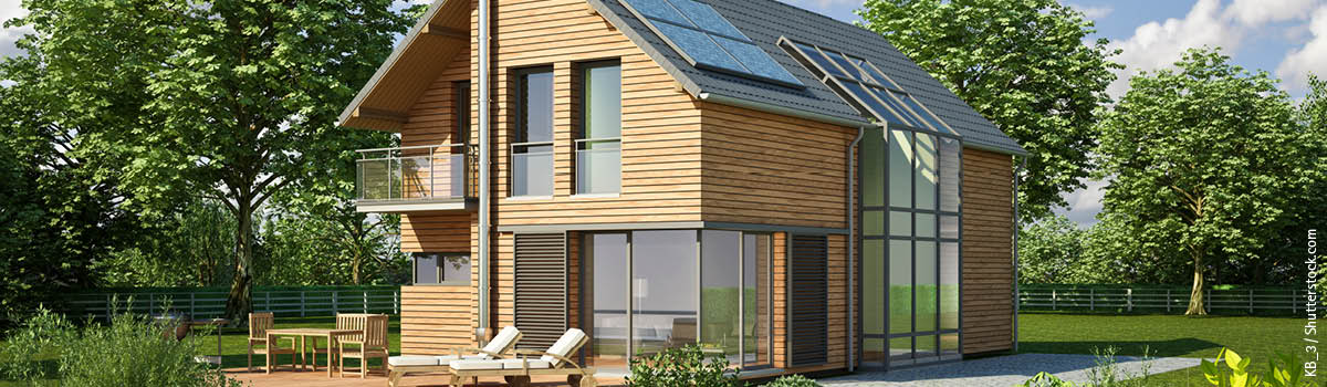 Modernes Haus mit Holzfassade, großen Fenstern und Solarpanels steht in einem begrünten Garten
